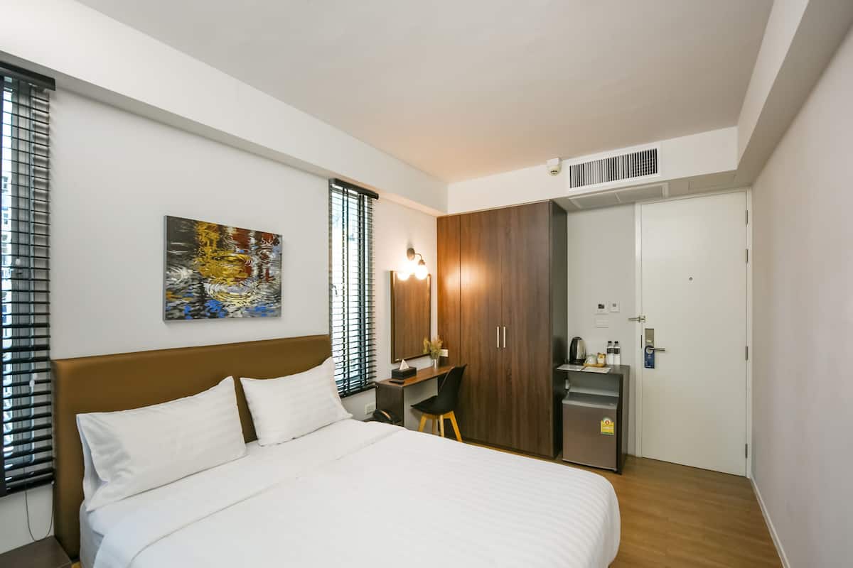 A hotel room with a bed, a desk, a chair, a wardrobe, and a small kitchenette.