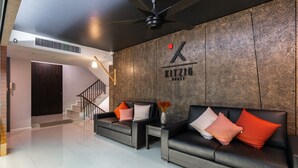 A modern living area with two black sofas, a small table, a vase with flowers, a ceiling fan, and a staircase leading to another room. - Kitzio House Hotel (Bangkok)