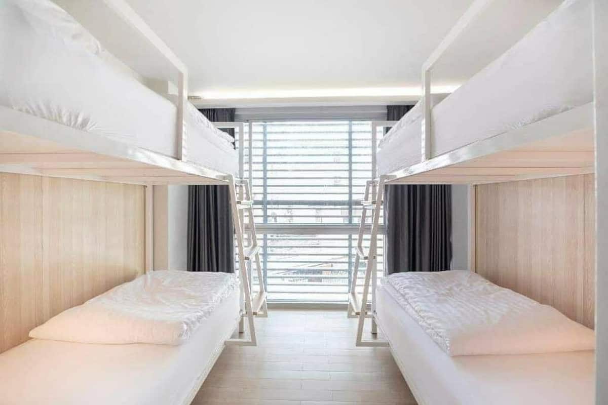 A hotel room with bunk beds, a wooden floor, and a window with blinds.