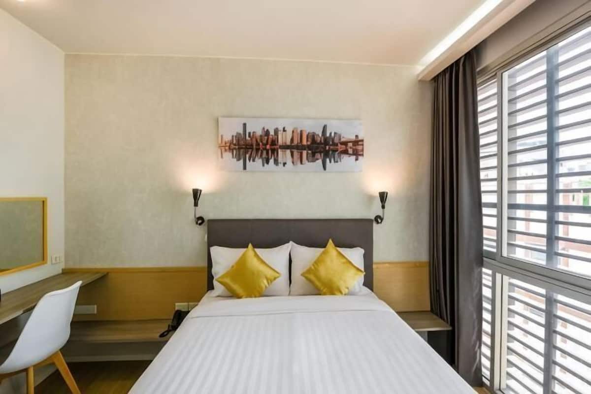A hotel room with a bed, two bedside lamps, a desk, a chair, and a window with blinds.