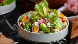 A bowl of salad with lettuce, bacon, and hard-boiled eggs.