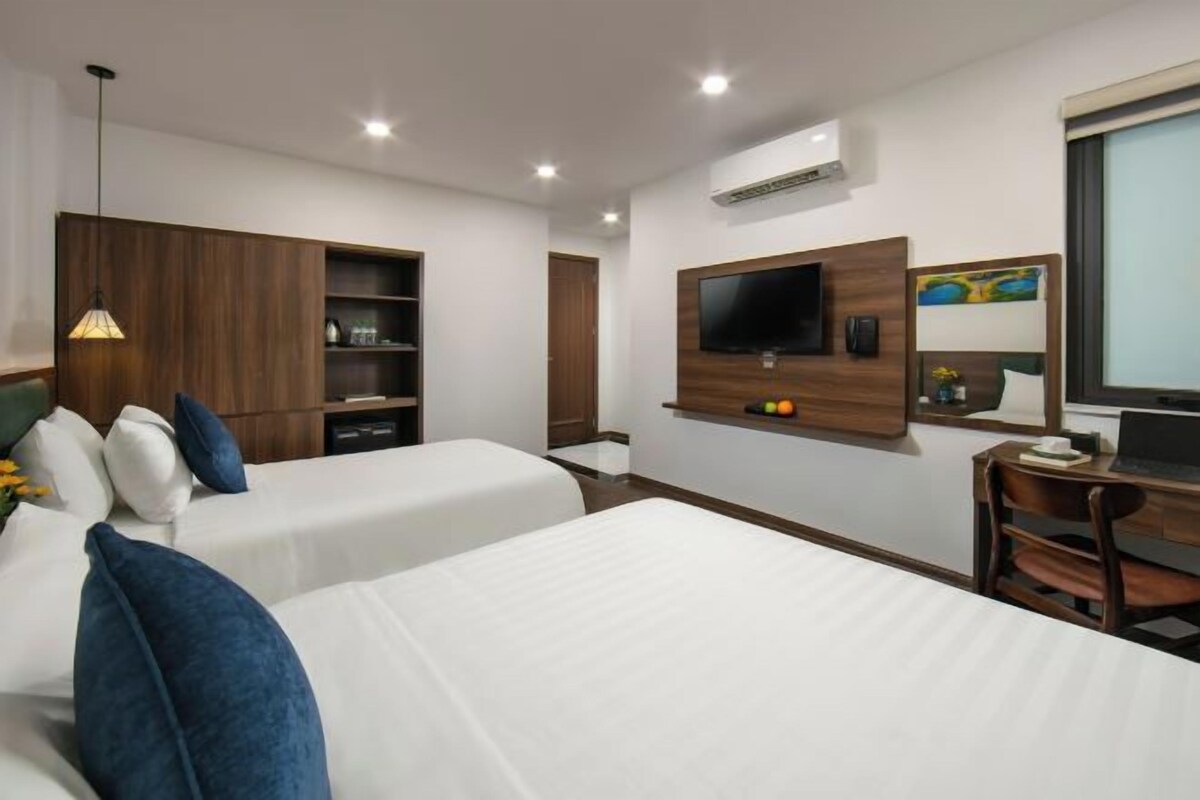 Camera d'albergo con due letti, una TV a muro, una scrivania con una sedia e un armadio in legno.