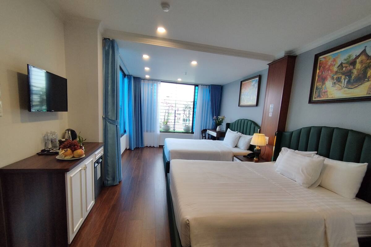 A hotel room with two beds, a desk with a computer, a TV, and a window with curtains.