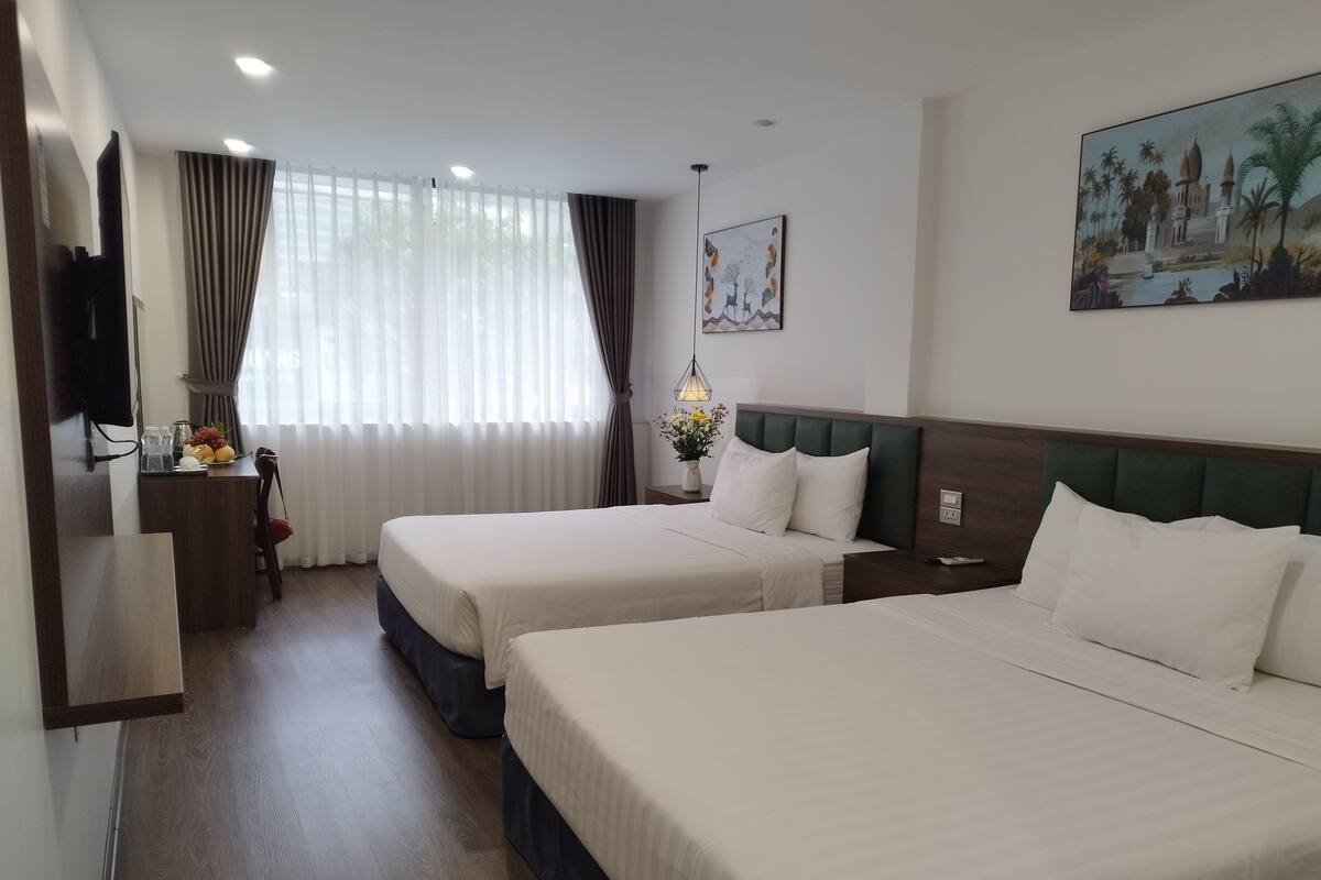 A hotel room with two beds, a desk, a chair, a TV, and a painting on the wall.