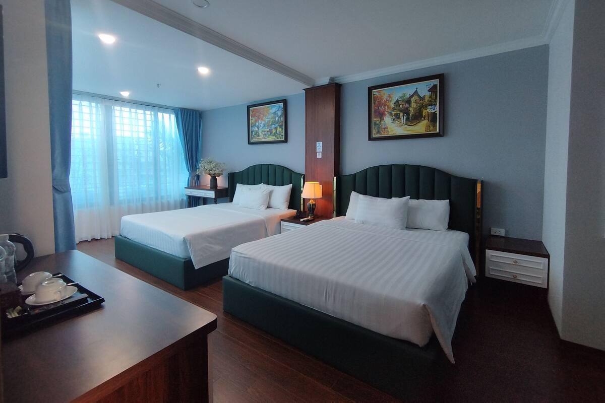 A hotel room with two beds, a desk, a chair, and a window with curtains.