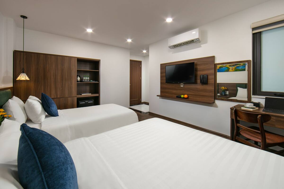 A hotel room with two beds, a desk with a laptop, a TV, and a wooden wardrobe.