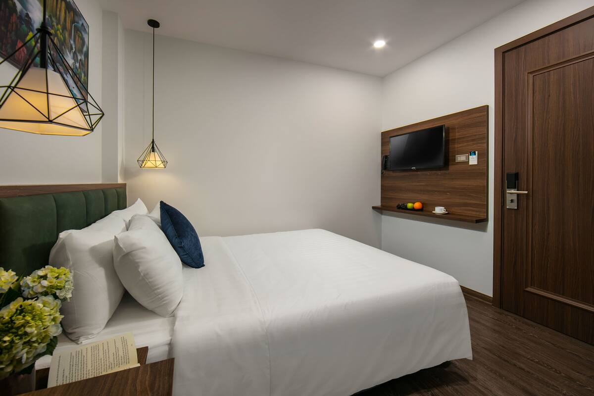 A neatly made bed with white bedding and blue pillows, a wall-mounted TV, and a wooden door.