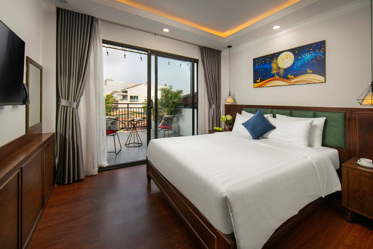 A hotel room with a large bed, a flat-screen TV, a balcony with a view, and a painting on the wall.