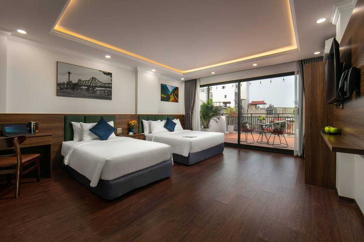A hotel room with two beds, a desk, a TV, and a balcony with a view.