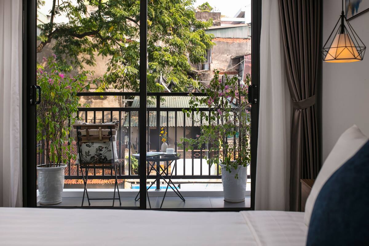 A balcony with a table and chairs, potted plants, and a view of buildings and trees.