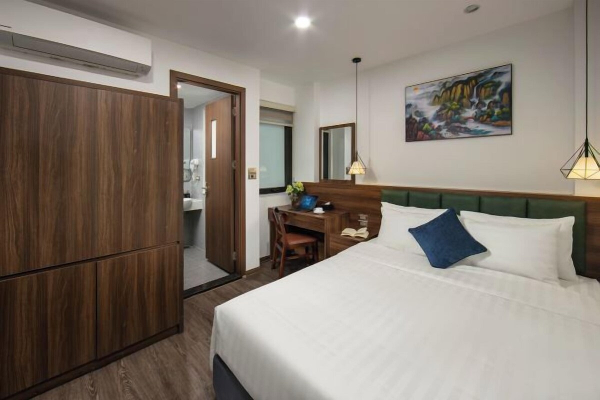 Una camera d'albergo con un letto, una scrivania, una sedia, un armadio, un quadro appeso al muro e uno specchio.