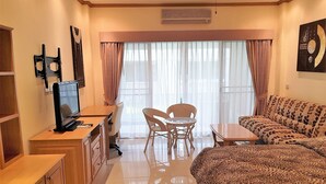 Une chambre d’hôtel comprenant un lit, un bureau avec un ordinateur, une chaise, un canapé et une grande fenêtre avec des rideaux.