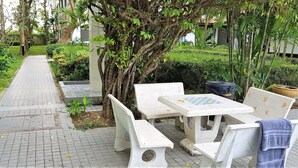 Un chemin pavé mène à un espace aménagé avec des bancs et une table, le tout entouré de verdure et d’arbres.