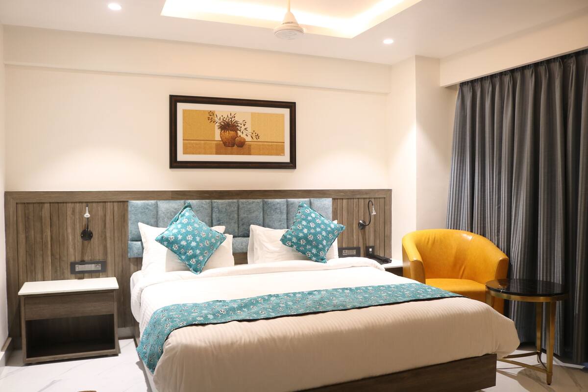 Hotelkamer met een groot bed, nachtkastje, stoel, klein tafeltje en een lijst aan de muur.