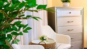 A room with a white upholstered chair, a small round table with a wicker basket, and a filing cabinet. - Sweet Home Georgia Luxury (Duluth)