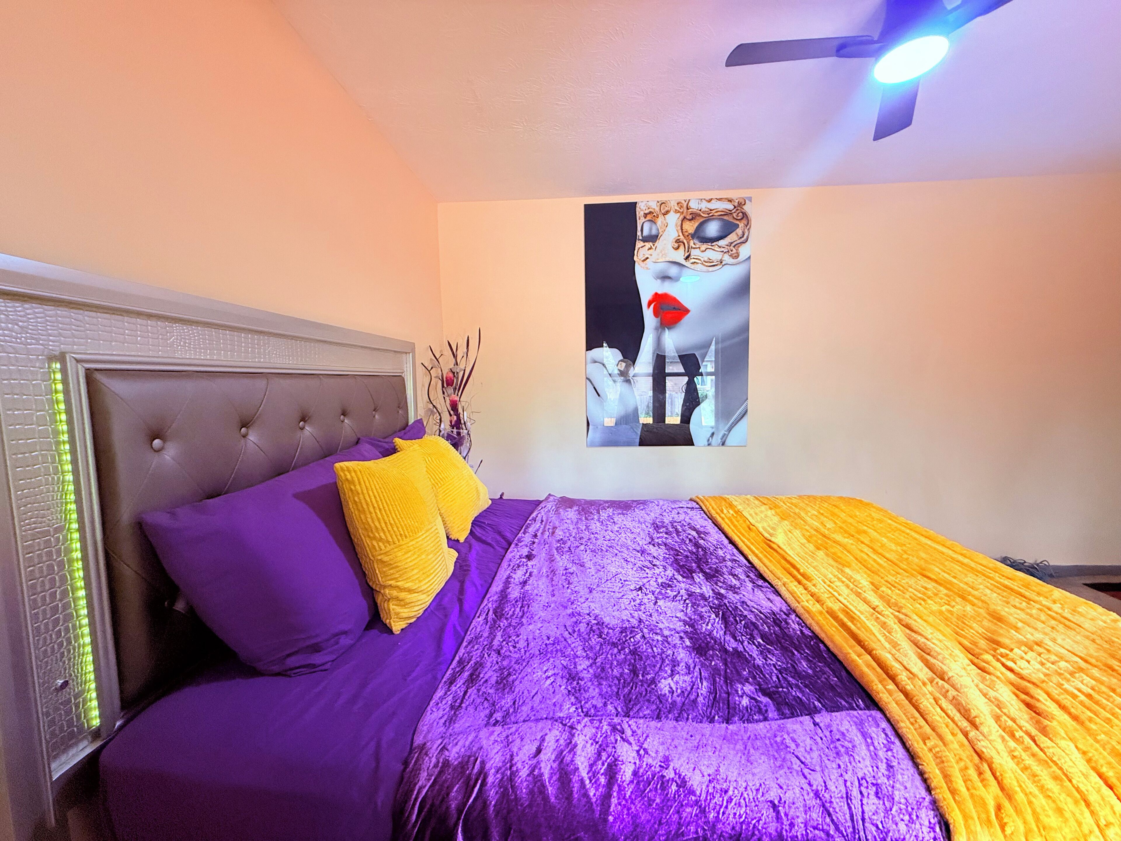 A bed with a tufted headboard, purple bedding, and a yellow throw.