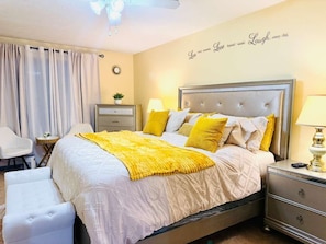 A bedroom with a bed, bedside tables, a nightstand, a chair, a desk, a lamp, a wall clock, and a decorative wall piece. - Sweet Home Georgia Luxury (Duluth)