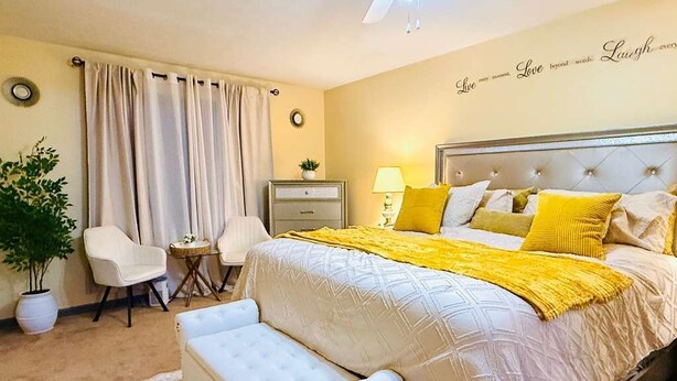 A bedroom with a bed, bedside table, lamp, chair, and a wall with a decorative sign. - Sweet Home Georgia Luxury (Duluth)