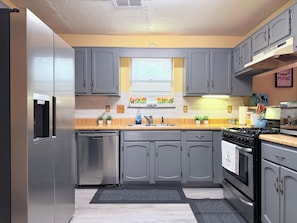 A kitchen with grey cabinets, a stainless steel refrigerator, a sink, a stove, and a window with flowers. - Sweet Home Georgia Luxury (Duluth)