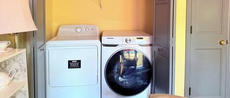 Une buanderie équipée de deux machines à laver et d’un sèche-linge, d’une étagère contenant des produits de lessive et d’un panneau indiquant qu’il s’agit d’un établissement en libre-service, ouvert 24 heures sur 24.