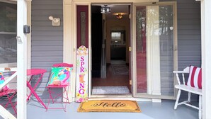 A porch with a 'HELLO' mat, a 'SPRING' sign, a red chair, and a table. - Sweet Home Georgia Luxury (Duluth)