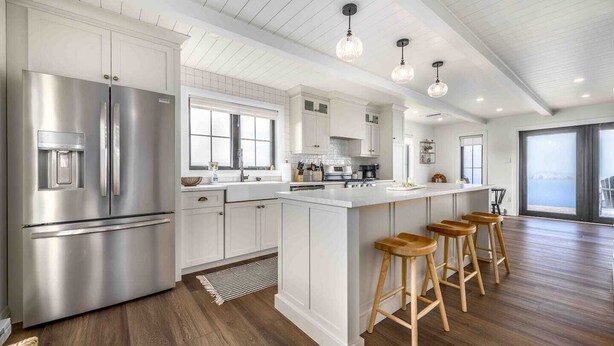 Una cocina moderna con armarios blancos, electrodomésticos de acero inoxidable y taburetes de bar de madera.
