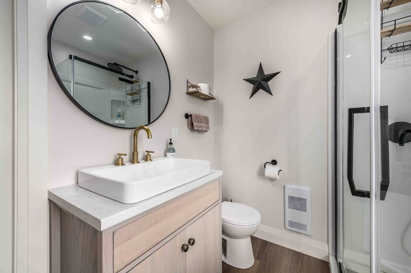 Een moderne badkamer met een witte wasbak, gouden kranen, een grote spiegel, een toilet, een douche en een sterren decoratie aan de muur.