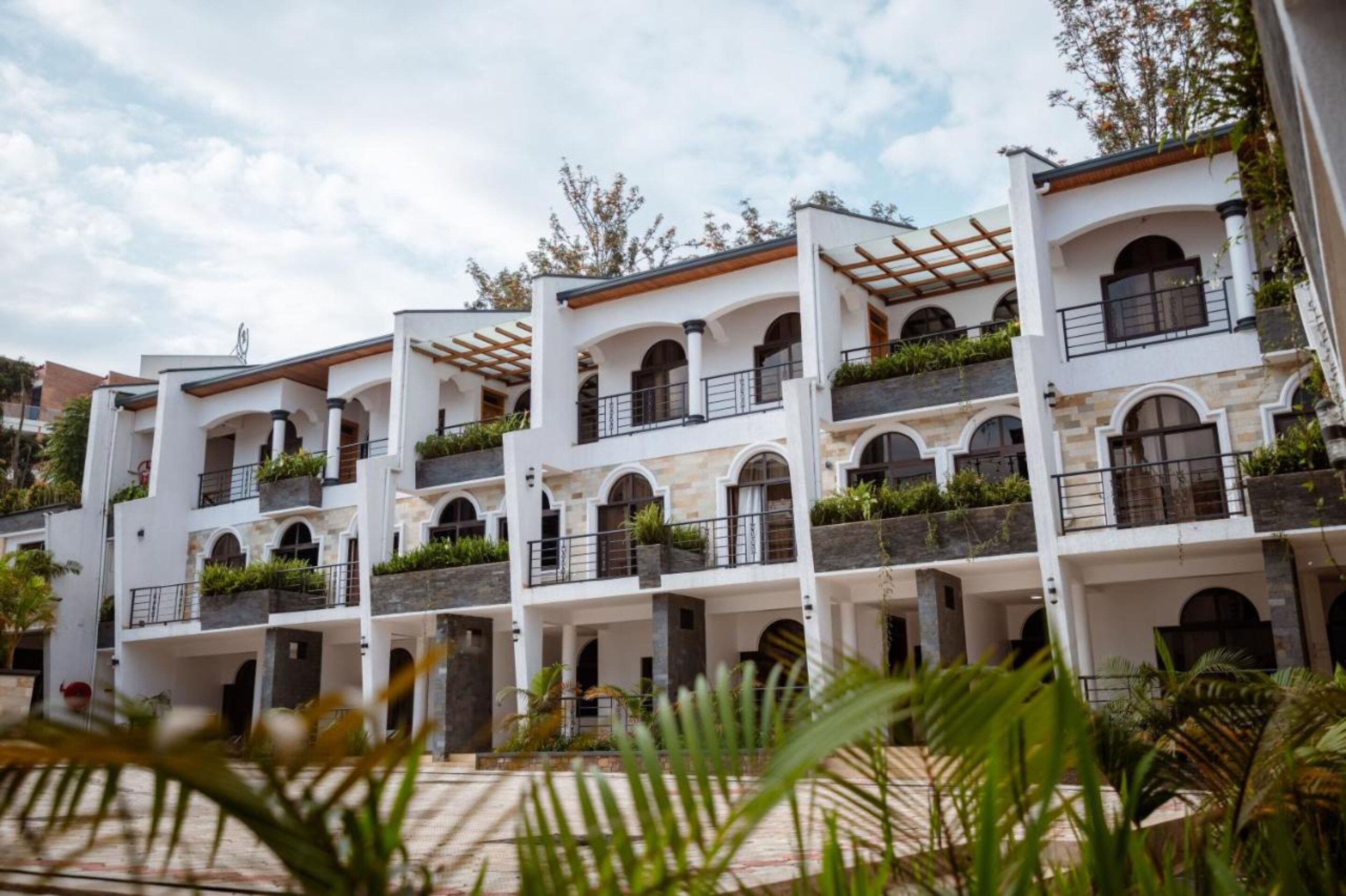 Un hôtel à plusieurs étages, avec des murs extérieurs blancs, des fenêtres en arc de cercle et des balcons ornés de plantes.