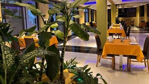 Un restaurante con mesas dispuestas para comer, rodeado de grandes macetas con plantas.