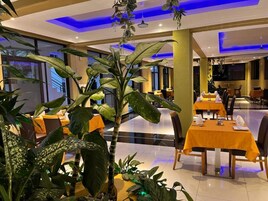 Un restaurant où les tables sont dressées pour le service, entouré de grands pots de plantes.