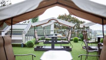 An outdoor patio area with a covered seating arrangement, tables, and chairs.