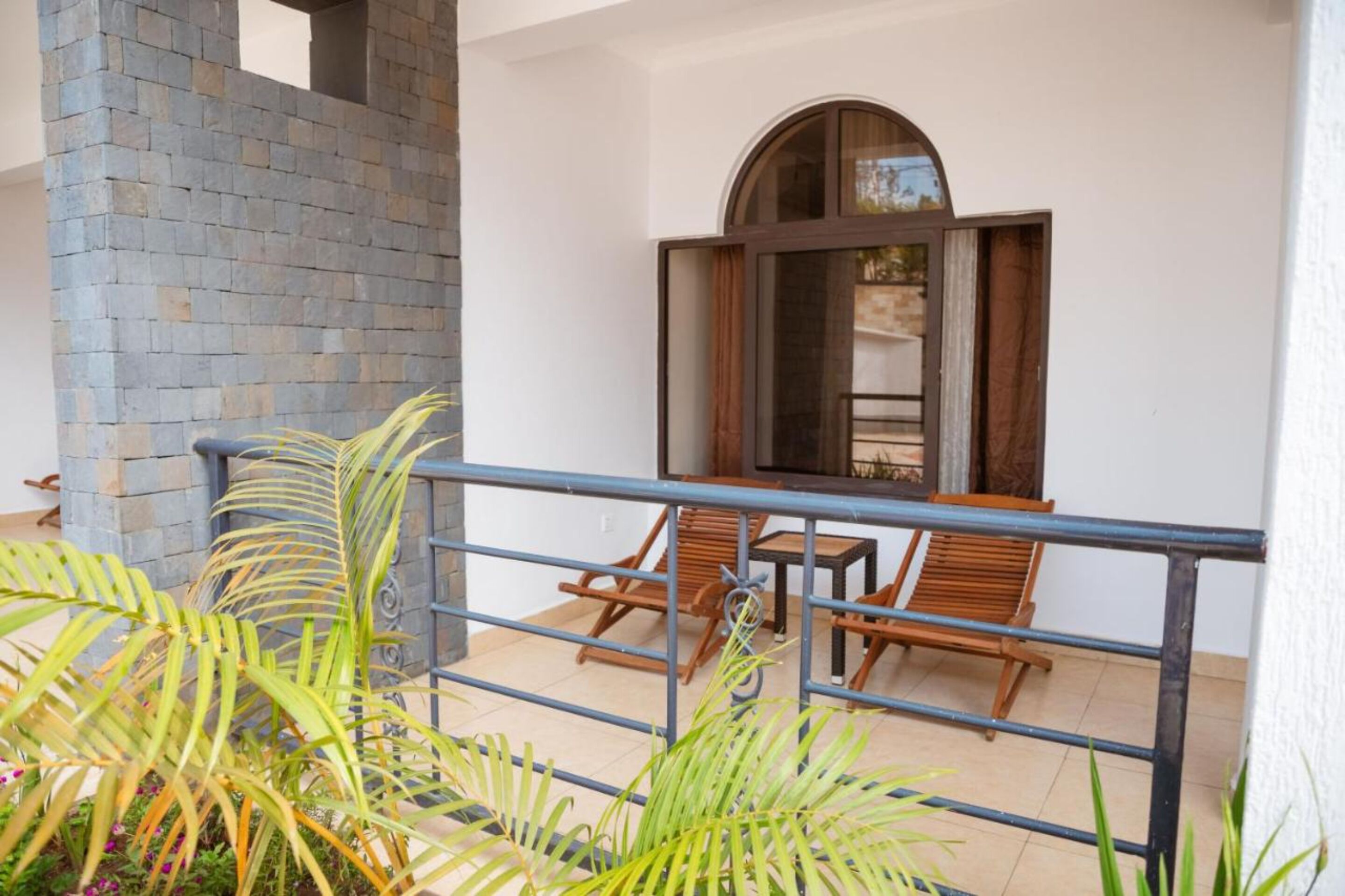 Un balcón con pared de piedra, sillas de madera, una mesa y plantas en macetas.