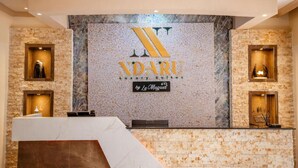 Un área de recepción con una pared de mármol, el logotipo de 'NADARU Luxury Suites by Le Muguet' y dos vitrinas con objetos.