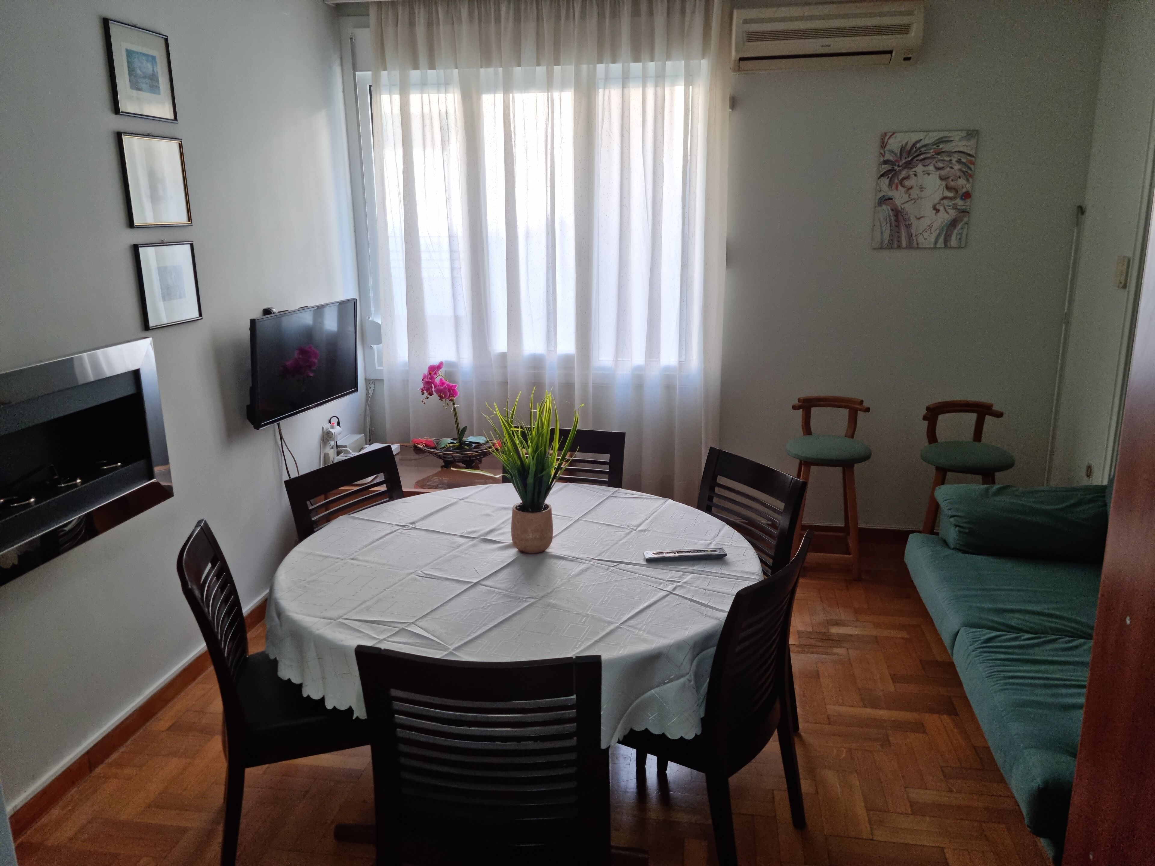 A dining area with a round table, chairs, a TV, and a couch.