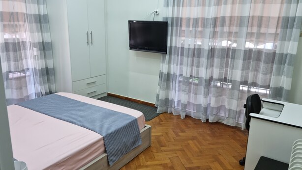 Ein Schlafzimmer mit Bett, Schreibtisch, Stuhl, Fernseher und Kleiderschrank.
