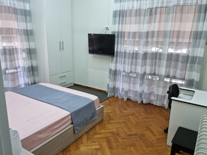 Un dormitorio con cama, escritorio, silla, televisor y armario.