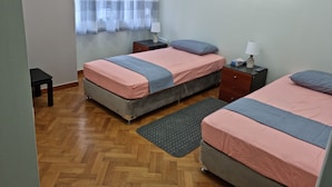Ein Schlafzimmer mit zwei Betten, einem Fenster mit Vorhängen, einem Nachttisch, einer Lampe und einem Gemälde an der Wand.