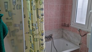 Ein Badezimmer mit einer Badewanne, rosa Kacheln, einem Fenster und einem Duschvorhang mit Besteck-Motiven.