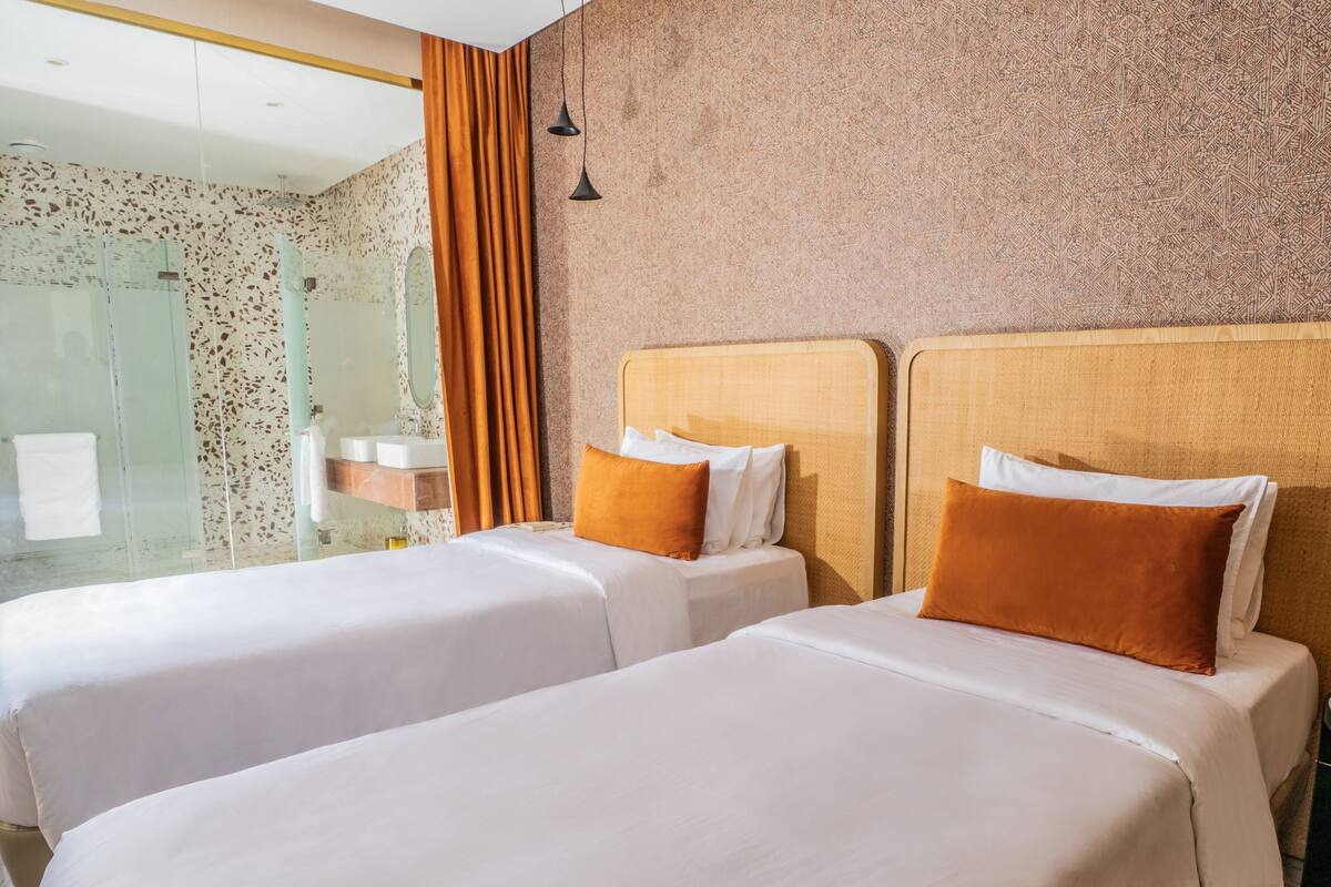 Une chambre d’hôtel avec deux lits, un espace douche et un mur à texture.
