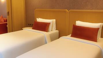 Dos camas individuales con sábanas blancas y almohadas rojas, un cabecero de madera y una pared con textura.