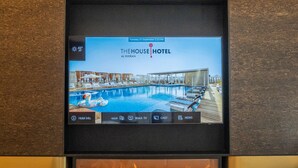 Eine Hotelhalle mit einem Flachbildfernseher, der den Hotelnamen zeigt, einem Poolbereich, einem Kamin und einer Sitzecke mit einer Zeitschrift und einer Pflanze.