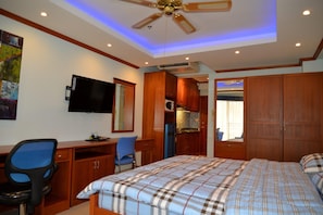 A bedroom with a bed, a desk, a chair, a television, and wooden cabinets.