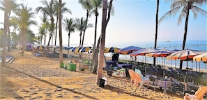 A beach with rows of colorful umbrellas and chairs, palm trees, and a view of the sea. - Jomtien Beach Condo 5th Floor Studio Apartment (Pattaya)
