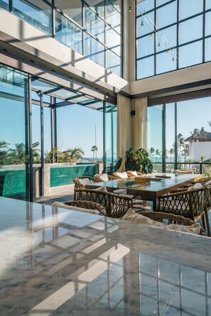 Un espace intérieur moderne avec un mur de verre donnant sur une piscine et des palmiers.