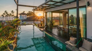 Una casa moderna con un balcón acristalado, piscina y vistas al atardecer.