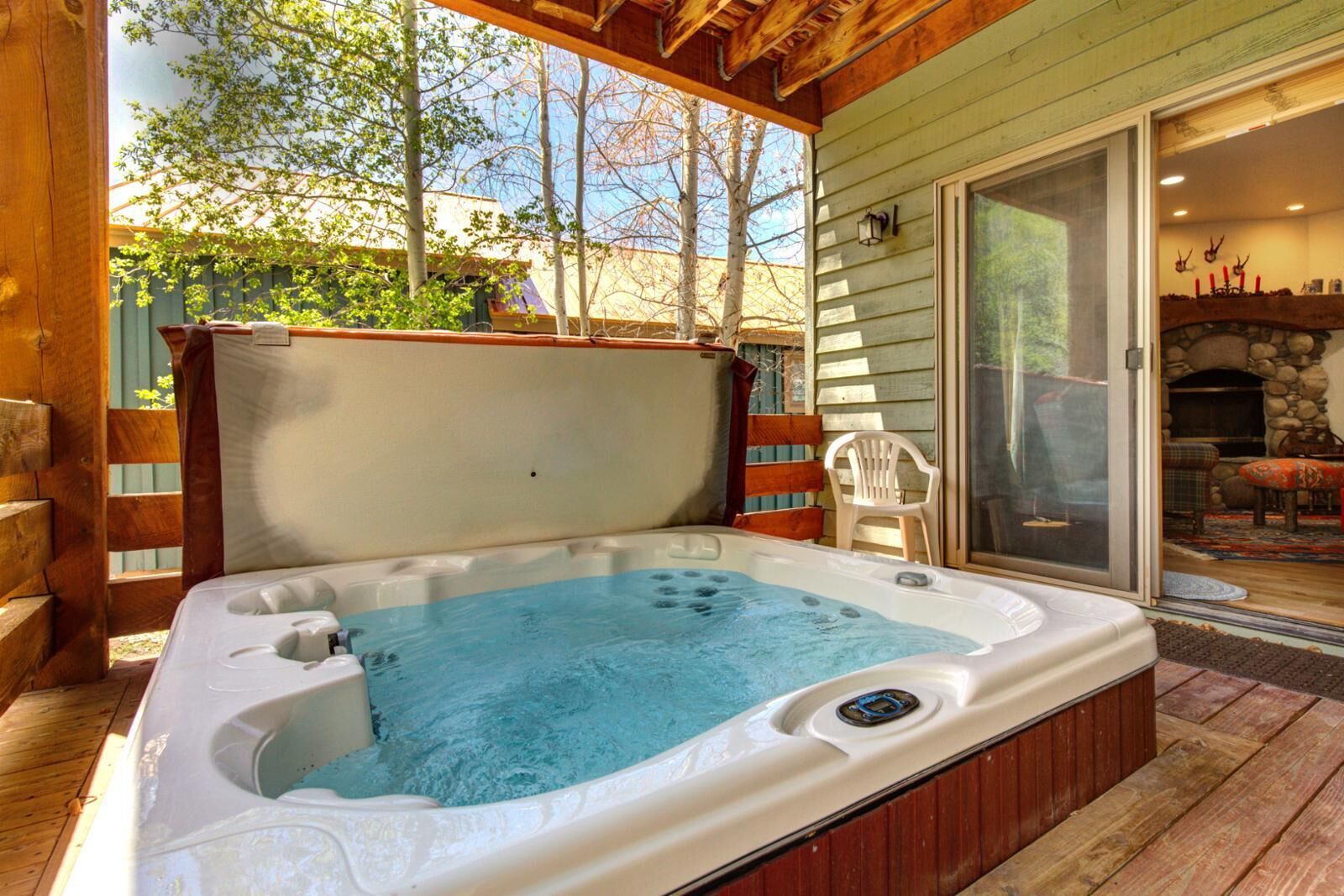 Un bain à remous situé sur une terrasse en bois, avec vue sur les arbres et une cheminée en pierre.