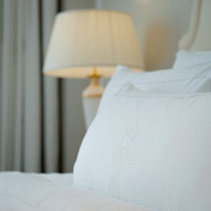 A neatly made bed with white linens and a pillow with an embossed logo. - The Plaza Doha, LXR Hotels & Resorts (Doha)