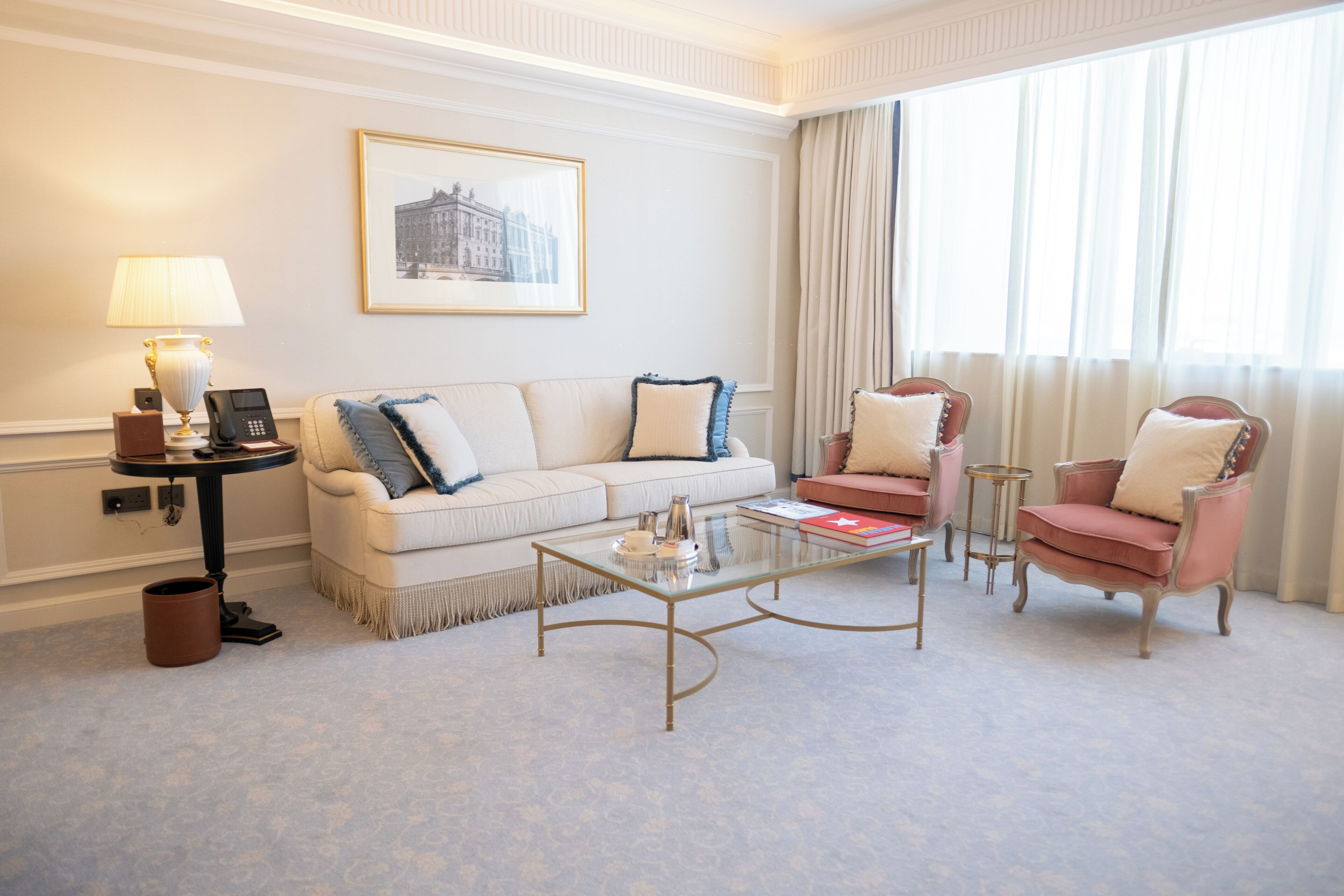 Een hotelkamer met een bank, fauteuils, een bijzettafeltje, een lamp, een telefoon en een ingelijst schilderij aan de muur.