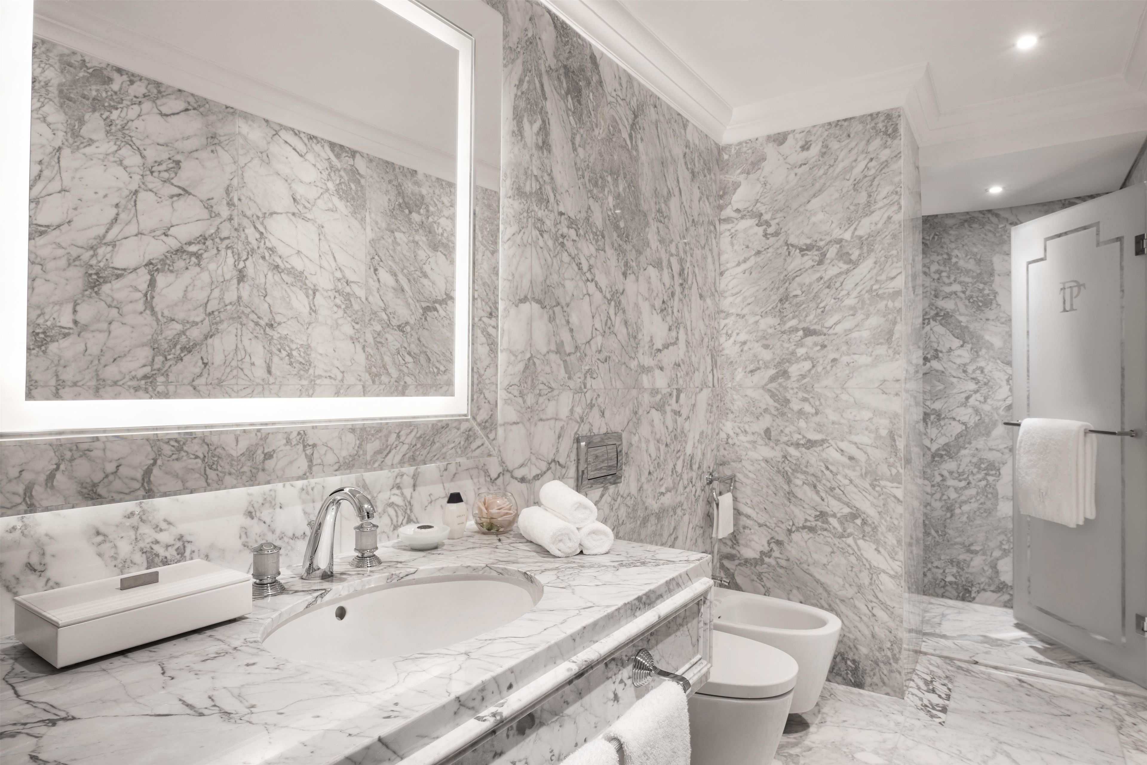 Un baño con lavamanos de mármol, un espejo grande y un inodoro.