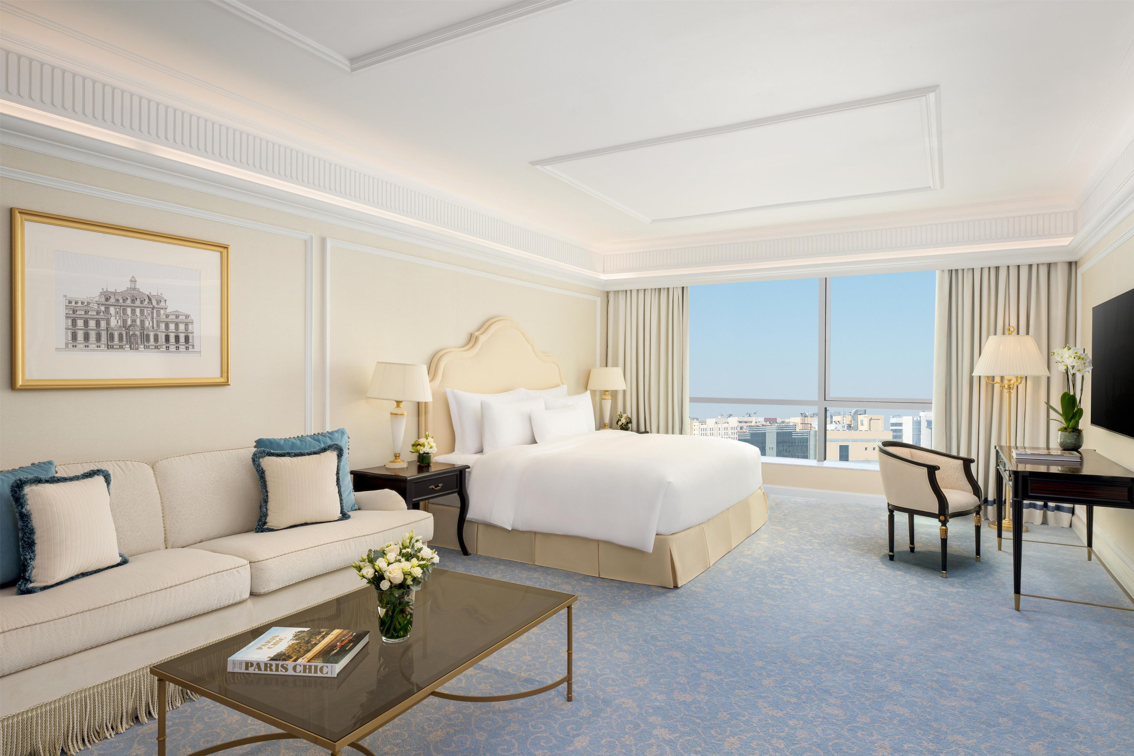 A hotel room with a bed, a sofa, a coffee table, a desk, and a television.
